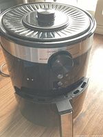 Front view of the air fryer showing temperature dial, temperature markings, and indicator lights on a black and silver unit