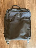 Full front view of the medium black fabric suitcase showing wheels, handle, and front zippered pocket