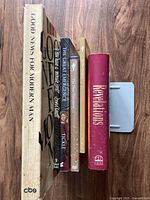 Side view of five books and one DVD, showing titles: Good News for Modern Man, The Great Emergence, two copies of The New Testament, Revelations.