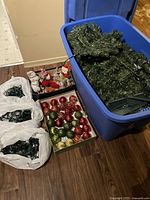 Wide view of artificial Christmas tree branches stored in a blue plastic bin, multiple Christmas light strings in bags, and several boxes of red, green, and gold Christmas ornaments.