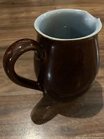 Brown stoneware jug with handle and visible minor chip near the spout on wooden surface