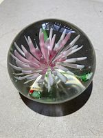 Front angle showing clear glass paperweight with pink and white floral petals and green leaves inside.