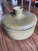 Closed view of the handmade Acorn Pottery lidded bowl showing the lid's knob handle and speckled green/brown clay surface.
