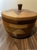 Full view of the closed wooden bowl with geometric inlay and knob lid on wood floor.