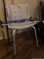Full view of beige plastic shower chair with metal legs and blue canes leaning on it