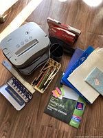 Wide view of lot showing paper shredder, metal ruler, colored pencils, mailing labels, binders/folders, pencil cup, hole punch, and stationery items