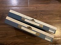 Two Smith-Victor photographic slide storage cases placed horizontally on a wood floor showing their front and top sides with metal clasps.