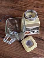 Overall view of the Osterizer blender components including the base, glass pitcher, and lid on a wooden surface.