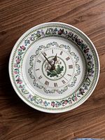 Front view of round ceramic clock with floral botanical pattern and Roman numerals on white base.