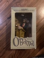 Front view of the Barack Obama toy in original box showing figure behind window and printed text on box front.