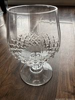 Close-up photo of single clear stemmed glass with diamond textured pattern on the bowl, standing upright on wooden floor, showing overall shape and design.