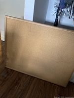 Full view of rectangular solid cork board with wood frame leaning against a wall.
