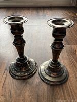 Pair of tarnished silver on copper candle holders with traditional design shown on wooden floor.