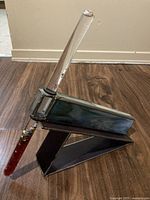 Kaleidoscope positioned upright on its matching stained glass stand. The kaleidoscope housing is seen with blue-green stained glass panels and a transparent glass tube handle containing colorful beads.