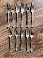 Set of eleven vintage silver-plated dessert forks laid out on wooden surface, showing overall condition and pattern on handles.