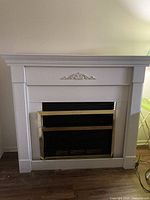 Full view of a white wooden fireplace mantel with decorative molding and an electric fireplace insert with brass trim in front.