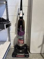 Full front view of Bissell vacuum standing vertically against wall, showing hose, handle, and dustbin area