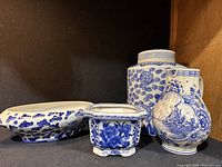 Four blue and white ceramic decor items arranged together including two vases, a bowl, and a planter.