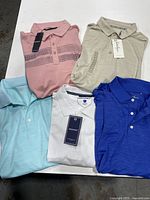All five shirts folded on white table showcasing different colors and labels.