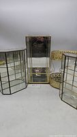 Photo showing all four display pieces: tall glass case centrally placed, two smaller multi-panel glass cases on either side, and round two-tier decorative brass tray at the back right.