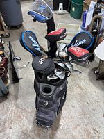 Photo of top of golf bag showing multiple golf clubs with branded head covers including Adams, IDEA, and iRT