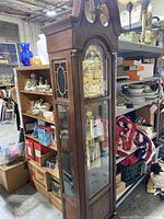 Full view of the tall grandfather clock in a warehouse setting.