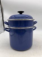 Blue Le Creuset pasta pot with strainer insert stacked inside and lid placed on top, front view showing pot and handle details.