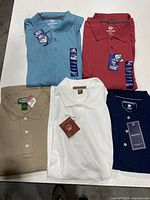 Five new short sleeve polo shirts in various colors laid out on a white surface, showing tags and collars.
