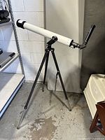 Full view of the Montgomery Ward astronomical telescope mounted on a black tripod in indoor space.