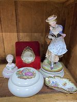 Porcelain Victorian style lady figurine with round base, round floral trinket box with lid, porcelain bust trinket dish, and a small dish with a red velvet backing frame behind