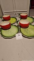 Four sets of tomato-shaped cups paired with lettuce leaf-shaped plates displayed showing detailing of tomato cups and lettuce leaf plates.