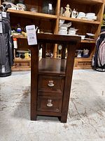 Front view of wooden side table showing two drawers with metal handles and open middle shelf