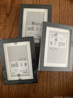 Three black IKEA RIBBA frames stacked on wood floor, showing packaging and labels.