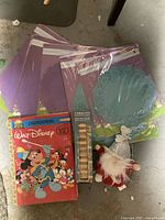 Photo showing six packages of blue and purple paper doilies, Walt Disney coloring book, wooden building block tower game in its box, and gnome Christmas stuffed toy.