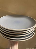 Stack of six blue-grey Denby luncheon plates held in hand showing top blue-grey surface