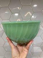 Side view of the vintage green Fire King jadite glass bowl showing the curved ribbed swirl pattern and translucent pale green color.