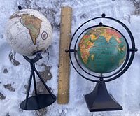 Two globes placed on snow with a wooden ruler, showing approximate sizes and stand styles
