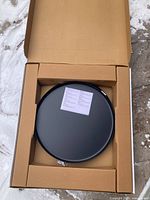 Round black metal tabletop inside original packaging with an instruction sheet on top.