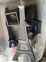 Top view of three metal Eiffel Tower models laid in a container, showing the black, brown, and silver colors and lattice construction.