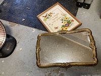 View of ornate gold-tone resin framed mirror with decorative flourishes on a concrete floor.