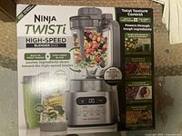 Front of the box showing complete blender setup with pitcher filled with fruit and smoothie images, highlighting the twist tamper and high-speed blade technology.
