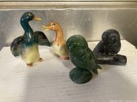 Four bird figurines including ceramic ducks, soapstone owl, and black owl salt and pepper set