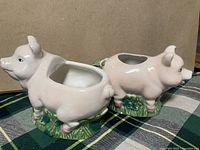 Two vintage light pink ceramic pigs, a creamer and sugar bowl, on dark and green plaid cloth.