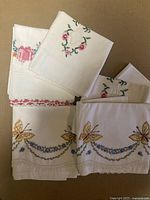 Photo of five folded white pillowcases showing floral wreath embroidery and butterfly motifs with lace edges.