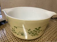 Oval Pyrex casserole dish with beige and green floral vine Shenandoah pattern, spouted side shown, interior white and appears cleanable.