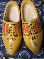 Top view of the pair of Dutch wooden shoes showing yellow color with red and black decorative paint and 'WETT GED' marking.