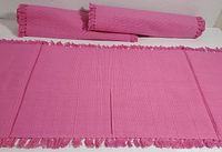 Three pink handwoven cotton table runners, two rolled and one laid flat, showing fringe detail and texture.