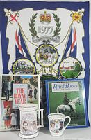 Full view of five Royal Family collectible items: large 1977 fabric piece, two books, and two commemorative mugs.