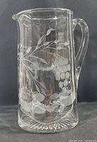 Front view of clear optic glass pitcher showing etched grape and leaf design with handle and pouring spout.