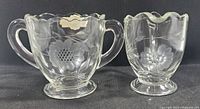 Photo of creamer and sugar bowl displaying clear crystalware with hand cut floral designs, scalloped rims, and pedestal bases